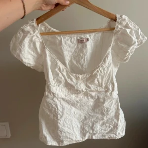 Vit blus med puffärmar - Charmig vit blus med korta puffärmar och v-ringning. Blusen har knappar framtill och är tillverkad i ett lätt och luftigt material, perfekt för varmare dagar.