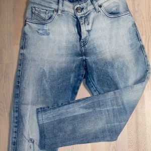 Blå jeans med slitningar - Snygga blå jeans med en cool tvättad look och slitningar på framsidan. De har en klassisk femficksdesign och knappgylf. Perfekta för en avslappnad stil.