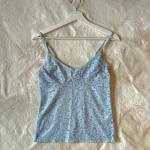 Ljusblå spetslinne - Säljer ett ljusblått spetslinne med smala axelband och v-ringning. Perfekt för för sig eller som ett lager under en tröja. Endast testad, men lappen är borttagen