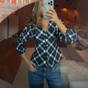 Rutig blus med knappar - Snygg rutig blus i svart och vit med knappar framtill. Blusen har trekvartsärmar och en v-ringad design!!🩵