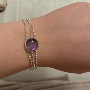 Silverarmband med lila sten - Elegant silverarmband med en lila sten i mitten. Armbandet har tre tunna kedjor som ger en stilren look. Perfekt för att lägga till en färgklick till din outfit. (Inte äkta silver!)