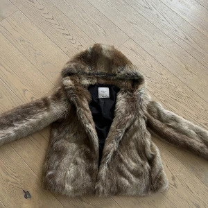 Brun pälsjacka från Zara i storlek M - Säljer en snygg brun pälsjacka från Zara Trafaluc. Jackan har en mysig huva och är perfekt för kyligare dagar. Den är långärmad och har en mjuk insida för extra komfort. Köpt Zara göteborg 