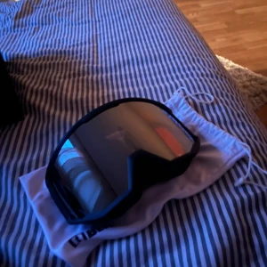 Svarta skidglasögon tonade - Säljer ett par snygga skidglasögon med färgen matt svart med orange och silver spegelglas. De har dubbel lins och är i nytt skick (aldrig använda). Perfekta för vinterns äventyr i backen! Kommer med en praktisk förvaringspåse.