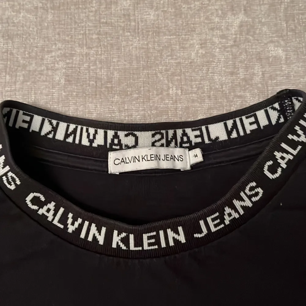 Snygg svart t-shirt från Calvin Klein Jeans med logotypdetaljer runt halsen och på ärmen. Perfekt för en stilren look.. T-shirts.