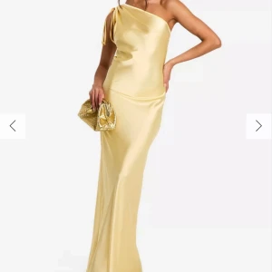 Gul  långklänning - ALDRIG ANVÄND! Elegant gul  långklänning i satin med en axelbandslös design. Klänningen har en smickrande passform och en stilren siluett, perfekt för festliga tillfällen.