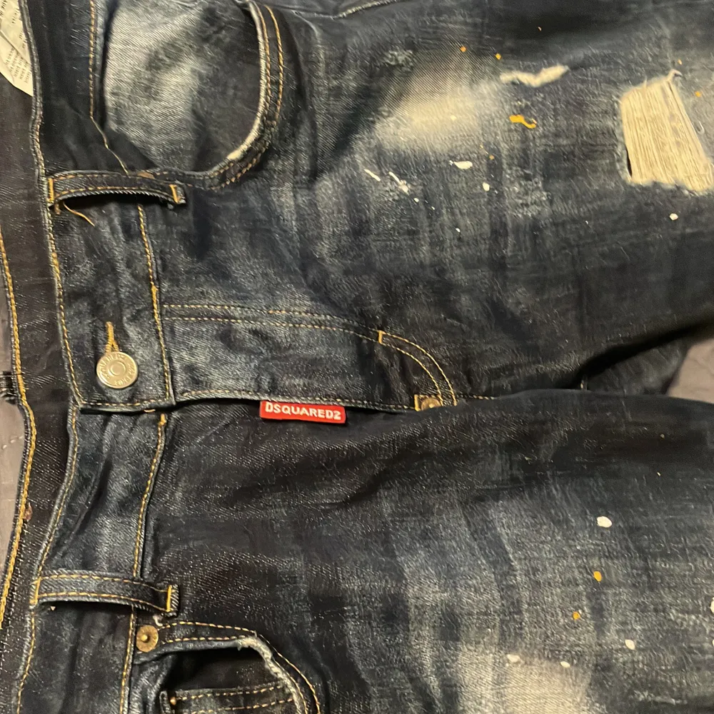 Säljer ett par snygga mörkblå jeans från Dsquared2. De har en cool distressed look med slitningar och färgstänk. Perfekta för en avslappnad stil! Jeansen har en normal passform och är i bra skick. Passar perfekt till både vardag och fest.. Jeans & Byxor.