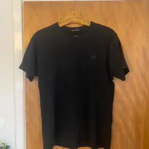 Snygg svart t-shirt från Acne Studios i 100% bomull. Perfekt för en stilren look. T-shirten har en liten logga på bröstet och är kortärmad. Passar till alla tillfällen!