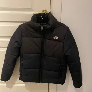 Säljer en svart dunjacka från The North Face. Jackan har en dragkedja framtill och är långärmad. Perfekt för kalla dagar med sin pufferdesign som håller värmen. Knappt  avänd. Nypris:2698:- säljes för 500:-