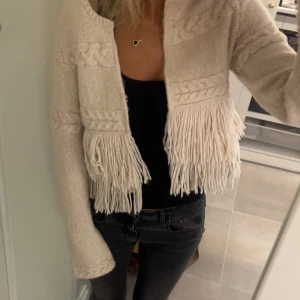Beige stickad kofta från Lindex - Säljer en beige stickad kofta från Lindex med flätade detaljer och fransar. Koftan har långa ärmar och har inga defekter.❤️