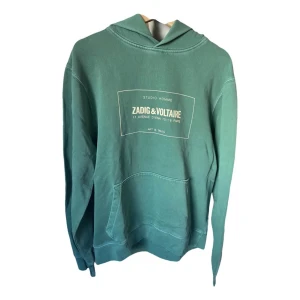Zadig & Voltaire hoodie - Snygg grön hoodie från Zadig & Voltaire med tryck på framsidan. Den har en klassisk känguruficka och en bekväm huva. Perfekt för en avslappnad stil.