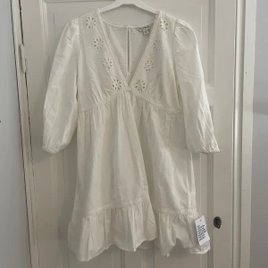 Vit klänning med broderade detaljer - Superfin vit klänning i linneblandning, med v-ringning och broderade blommor. Den har trekvartsärmar och en volangkant längst ner. Jättefin till vardags och andra finare tillställningar. Passar perfekt som studentklänning eller annan sommarklänning! Nypris: 519kr. Oanvänd. 🌺