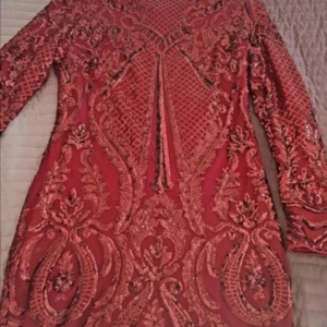 Röd glittrig klänning - Säljer en fantastisk röd klänning med glittriga detaljer och ett vackert broderat mönster. Klänningen har långa ärmar och en tight passform som framhäver figuren. Perfekt för festliga tillfällen där du vill sticka ut! ,eller till jul fest 