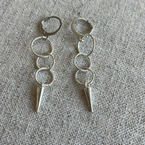 Silvriga örhängen med kedjor och koner - Säljer ett par coola silvriga örhängen med kedjor av ringar och spetsiga koner längst ner. Perfekta för att ge din outfit en edgy touch! 🖤