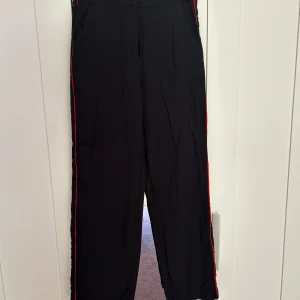 Svarta byxor med röd detalj - Mycket vackra byxor med röda linjer på sidorna.  Ser ut att vara ganska vida men sitter ganska tajt och fint i midjan och på baksidan🌸✨   Använda en gång ✨