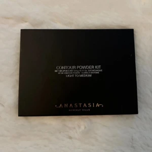 Contour Powder Kit från Anastasia Beverly Hills - Säljer ett Contour Powder Kit från Anastasia Beverly Hills i nyansen Light to Medium. Paletten innehåller sex olika puder för contouring och highlighting, perfekt för att skapa en definierad look. Den kommer i en snygg svart förpackning och är idealisk för både vardag och fest. Använd den för att framhäva dina bästa ansiktsdrag!