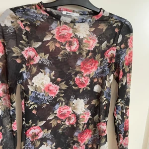 Blommig långärmad topp från Gina Tricot - Säljer en superfin långärmad genomskinlig topp från Gina Tricot med ett blommigt mönster i rosa, blått och vitt med svart som grund . Perfekt för både vardag och fest! Toppen är i ett tunt och bekvämt material.