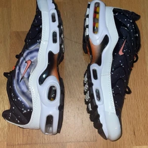 Nike Air Max med galaxmönster - Säljer ett par riktigt coola Nike Air Max med ett unikt galaxmönster. Skorna har en svart bas med vita stänk som ger en rymdliknande effekt. De har en synlig Air Max-dämpning i sulan och en orange swoosh-logga på sidan. Perfekta för dig som vill sticka ut!