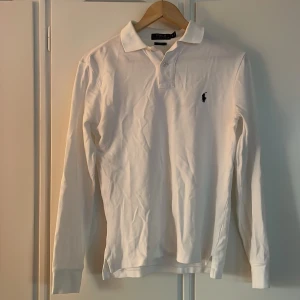 Ralph Lauren piké långärmad - Jag säljer en vit långärmad piké med blå logga ifrån Ralph Lauren i storlek S. Den är i mycket bra skick. Nypris ca 1500kr. 