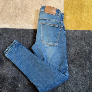 Blå jeans med läderdetalj - Säljer ett par snygga blå jeans med en cool läderdetalj på baksidan. De har en klassisk femficksdesign och en bekväm passform. Perfekta för både vardag och fest! Ny pris runt 1300kr👍bra kvalitet, aldrig använd!