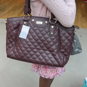 Brun quiltad axelväska från Fiorelli - Säljer en snygg vinröd axelväska från Feel. Väskan är quiltad och har en praktisk dragkedja upptill. Den är rymlig och perfekt för både vardag, skola och fest. Insidan är ljus och har flera fack för enkel organisering. Väskan har guldfärgade detaljer och rymmer en skoldator!