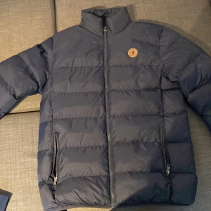 Blå dunjacka från Deerhunter - Säljer en snygg blå dunjacka från Deerhunter i storlek S. Jackan är perfekt för kyliga dagar med sitt quiltade mönster och dragkedja framtill. Den har en stilren design med ett litet märke på bröstet och två praktiska fickor med dragkedja. Perfekt för både vardag och utomhusaktiviteter!