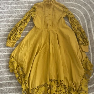 Gul klänning  - gul klänning med spetsdetaljer på ärmarna och längs nederkanten. Klänningen har en hög krage och knappar framtill, samt veckade detaljer på bröstet.😍😍 den är även öppen vid sidorna🤗