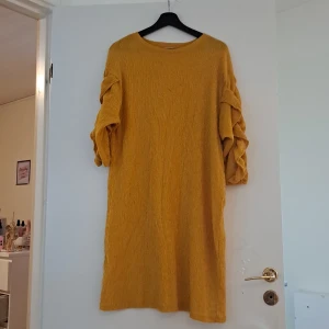 Gul klänning med volangdetaljer - Säljer en superfin gul klänning med volangdetaljer på ärmarna. Klänningen har en avslappnad passform och är perfekt för både vardag och fest. Materialet känns mjukt och bekvämt, och den har en härlig struktur som ger lite extra stil. Perfekt för höst och vår! Det har svart smuts framme men det kan ta bort med tvätt. 