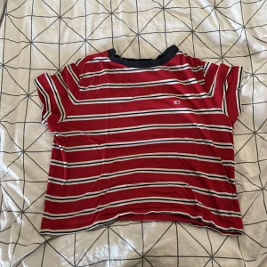 Röd och vit randig t-shirt från Tommy Jeans - Säljer en snygg röd och vit randig t-shirt från Tommy Jeans. Den har en avslappnad passform och korta ärmar, perfekt för en casual look. T-shirten är i bomull och har en liten logga på bröstet. Perfekt för sommardagar eller som en del av en lager-på-lager outfit!
