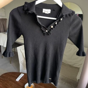 Svart tröja med pärlor - Jättesöt tröja med fina pärlor längs kragen. Kragen samt ärmarna har även som volanger längt ut på kanten. Knappt använd.