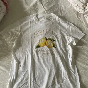 Tshirt - Vit t-shirt med tryck av citroner och texten "Capri Italia L'Isola del Sole Campania Region Tyrrhenian Sea". Storlek L