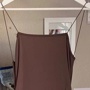 Brun klänning med knytdetalj - Säljer en snygg brun klänning med en unik knytdetalj i ryggen. Klänningen är ärmlös och har en tight passform som framhäver figuren. Perfekt för en fest eller en utekväll! Materialet känns mjukt och bekvämt mot huden.