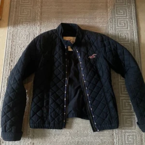 Svart quiltad jacka från Hollister - Säljer en snygg svart quiltad jacka från Hollister. Den har en dragkedja framtill och långa ärmar. Perfekt för höst och vår, med en stilren design som passar till det mesta. Jackan är i bra skick och redo för nya äventyr!