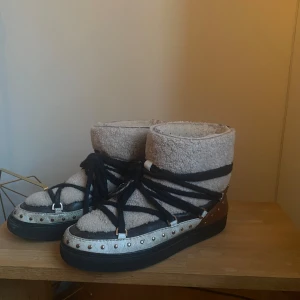 Boots från Inuikii - Säljer mina snygga och varma boots från Inuikii i mycket bra skick. De är i beigea och bruna med svarta detaljer, snörning och nitar runt sulan, Perfekta för vintern och hösten!