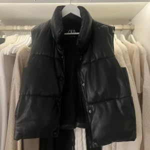 Svart dunväst från Zara - Säljer en snygg svart dunväst från Zara i storlek S. Västen har en hög krage och stängs med dragkedja och knappar. Perfekt för höst och vinter för en stilren look. 🖤