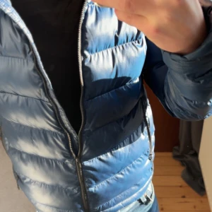 Blå pufferjacka - Säljer en snygg blå pufferjacka i mycket bra skick. Jackan har en dragkedja framtill och är perfekt för kyliga dagar. Den är långärmad och har en stilren design som passar både till vardags och fest. Perfekt för höst och vinter! Xs men sitter som s