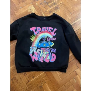 Ny sweatshirt med rymdmotiv alien svamlar psykadelisk M  - Cool svart sweatshirt med färgglatt rymdmotiv och texten 'Travel Around the World'. Tröjan har långa ärmar och är i ett mjukt material. Säljes pga för liten. St 38/40.