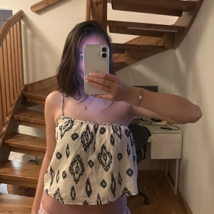 Topp - Säljer en superfin ärmlös topp med ett coolt mönster i svart och beige. Perfekt för sommardagar eller en avslappnad fest. Toppen har en luftig passform och tunna axelband.