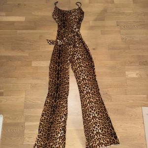 Leopardmönstrad jumpsuit - Säljer en supercool leopardmönstrad jumpsuit med smala axelband och knytband i midjan. Perfekt för en utekväll eller fest! Materialet känns mjukt och bekvämt, och den har en figurnära passform som framhäver formerna. Ett måste för garderoben om du älskar djurmönster!