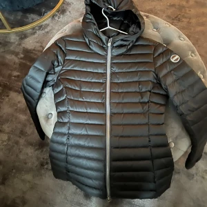 Svart dunjacka från Colmar - Säljer en snygg svart dunjacka från Colmar i storlek 42. Jackan har en dragkedja framtill och en mysig huva. Perfekt för kalla vinterdagar och håller dig varm och stilren. Passar både till vardags och lite finare tillfällen. 🖤