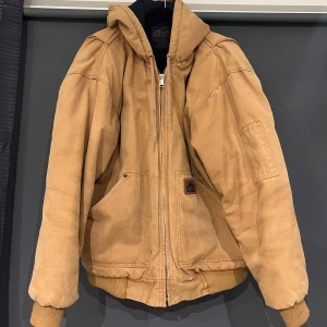 Beige jacka från Old Mill - Säljer en beige jacka från Old Mill i storlek L. Jackan har en dragkedja framtill och är tillverkad i bomull med polyesterfoder. Den har en huva och muddar vid ärmslut och nederkant för extra komfort. Perfekt för alla årstider!