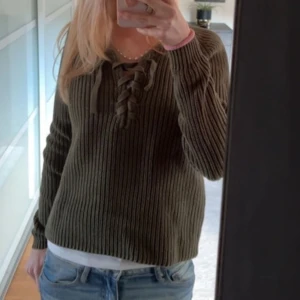 Olivgrön stickad tröja från Crocker - Säljer en superfin olivgrön stickad tröja från Crocker. Den har en snygg snörning framtill och är perfekt för höst och vinter. Tröjan är långärmad och har en skön, normal passform. ❤️