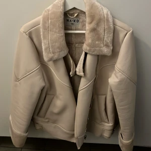 Beige jacka från NA-KD - Säljer en snygg beige jacka från NA-KD i mycket bra skick. Den har en mysig pälsliknande krage och dragkedja framtill. Perfekt för höst och vinter med sin varma och stilrena design. Jackan har långa ärmar och en normal passform. Passar perfekt till både vardag och fest!