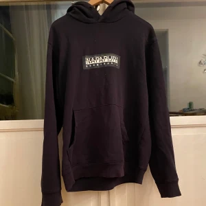 Mörkblå hoodie från Napapijri - Säljer en snygg mörkblå hoodie från Napapijri i storlek M. Den har en klassisk design med en stor ficka fram och en bekväm huva. Perfekt för kyliga dagar och passar till det mesta i garderoben. Kvaliteten är riktigt bra och den är i mycket bra skick.