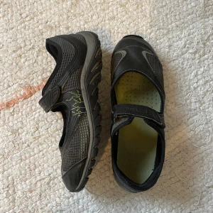 Sporty ballerina från Merrell - Säljer ett par svarta Mary Jane / ballerina / sport skor från Merrell. De har en praktisk kardborreknäppning och en robust sula med bra grepp. Skorna är perfekta för utomhusaktiviteter och har en ventilerande meshdesign för extra komfort. Perfekta för både träning och vardag!