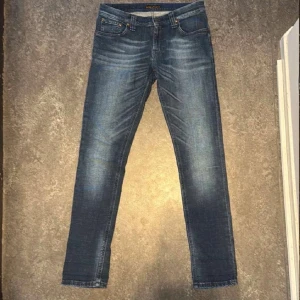 Blå jeans från Nudie Jeans - Säljer ett par snygga blå jeans från Nudie Jeans i bra skick. De har en klassisk straight fit och är perfekta för både vardag och fest. Jeansen har en snygg tvätt och är tillverkade i slitstarkt denim. Perfekt för dig som vill ha en stilren look!