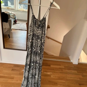Svartvit långklänning med mönster - Säljer en superfin svartvit långklänning med ett detaljerat mönster. Klänningen har smala axelband och är perfekt för sommardagar eller en avslappnad fest. Materialet känns lätt och luftigt, vilket gör den bekväm att bära hela dagen.