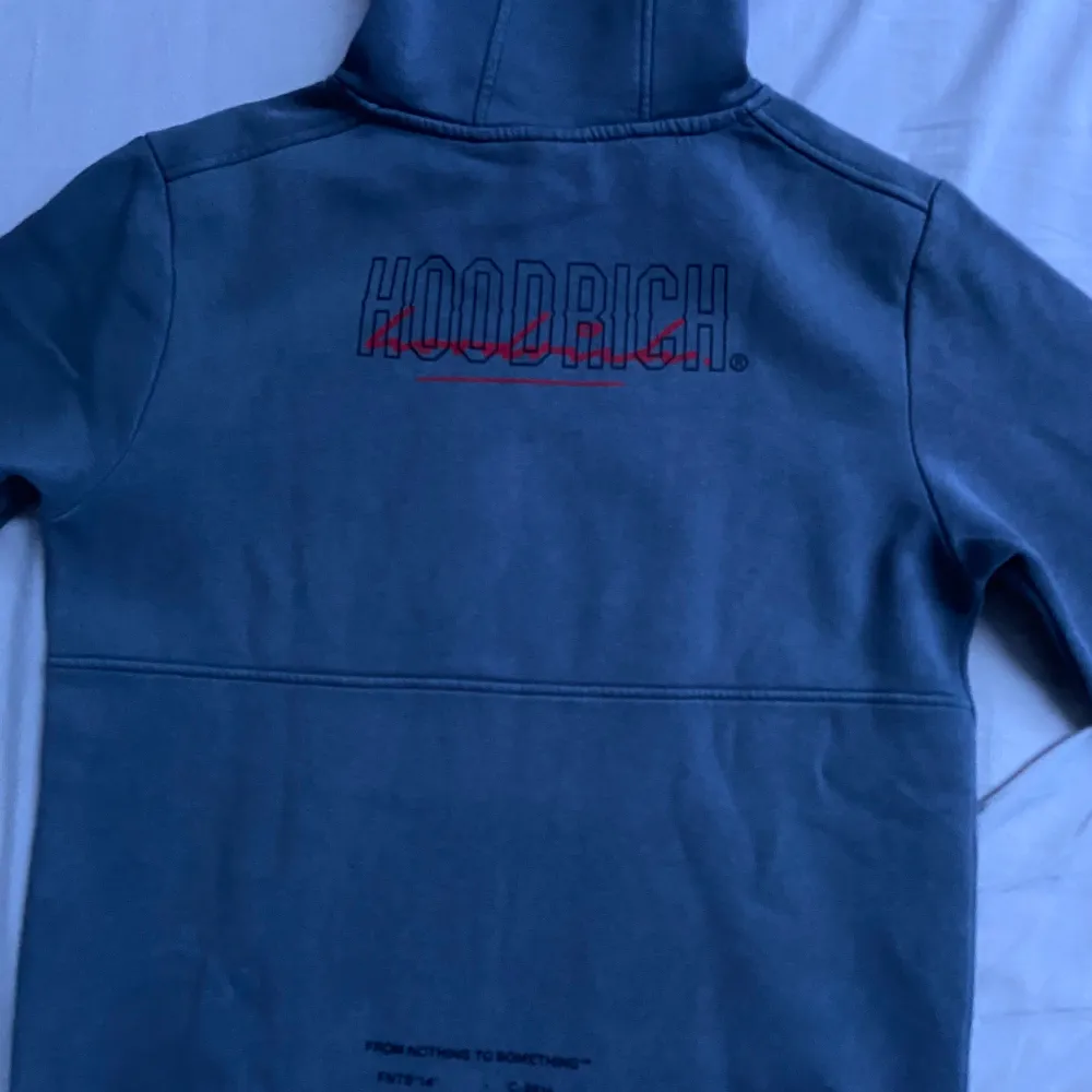 Säljer en snygg grå hoodie från Hoodrich med coola röda detaljer och tryck både fram och bak. Den har en klassisk känguruficka och en bekväm passform. Perfekt för en avslappnad stil eller streetwear-look. Passar bra till både jeans och joggers! Obs!! Den har sliten del på luvan (Syns på bilden) annars är den fläckfri . Tröjor & Koftor.