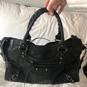 Svart handväska med dragkedja - Snygg svart handväska med coola detaljer. Den har en praktisk dragkedja och nitar som ger en edgy look. Perfekt för både vardag och fest! 🖤