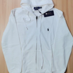Vit hoodie från Polo Ralph Lauren - Säljer en stilren vit hoodie från Polo Ralph Lauren i storlek M. Den har en dragkedja framtill och en klassisk broderad logga på bröstet. Perfekt för en avslappnad stil och passar till alla säsonger. Huvan ger extra mysfaktor! 🏷️