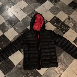 Svart dunjacka från Guess - Säljer en snygg svart dunjacka från Guess med rosa röd insida. Jackan har en dragkedja framtill och en huva för extra värme. Perfekt för kyliga dagar och ger en cool look. Passar både till vardags och lite finare tillfällen!!🥰❤️